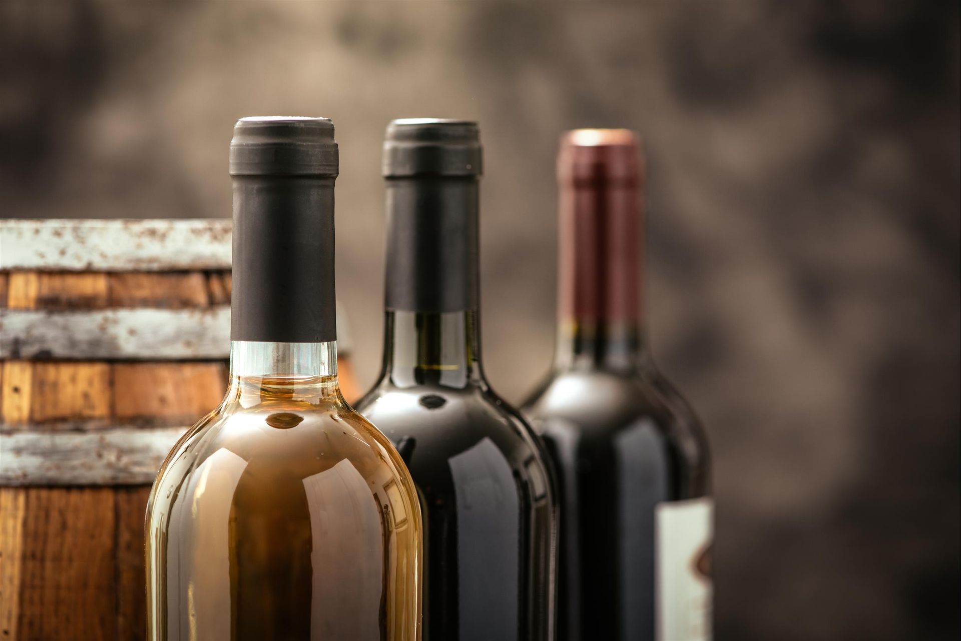 Three bottles of wine are sitting next to each other on a wooden barrel.