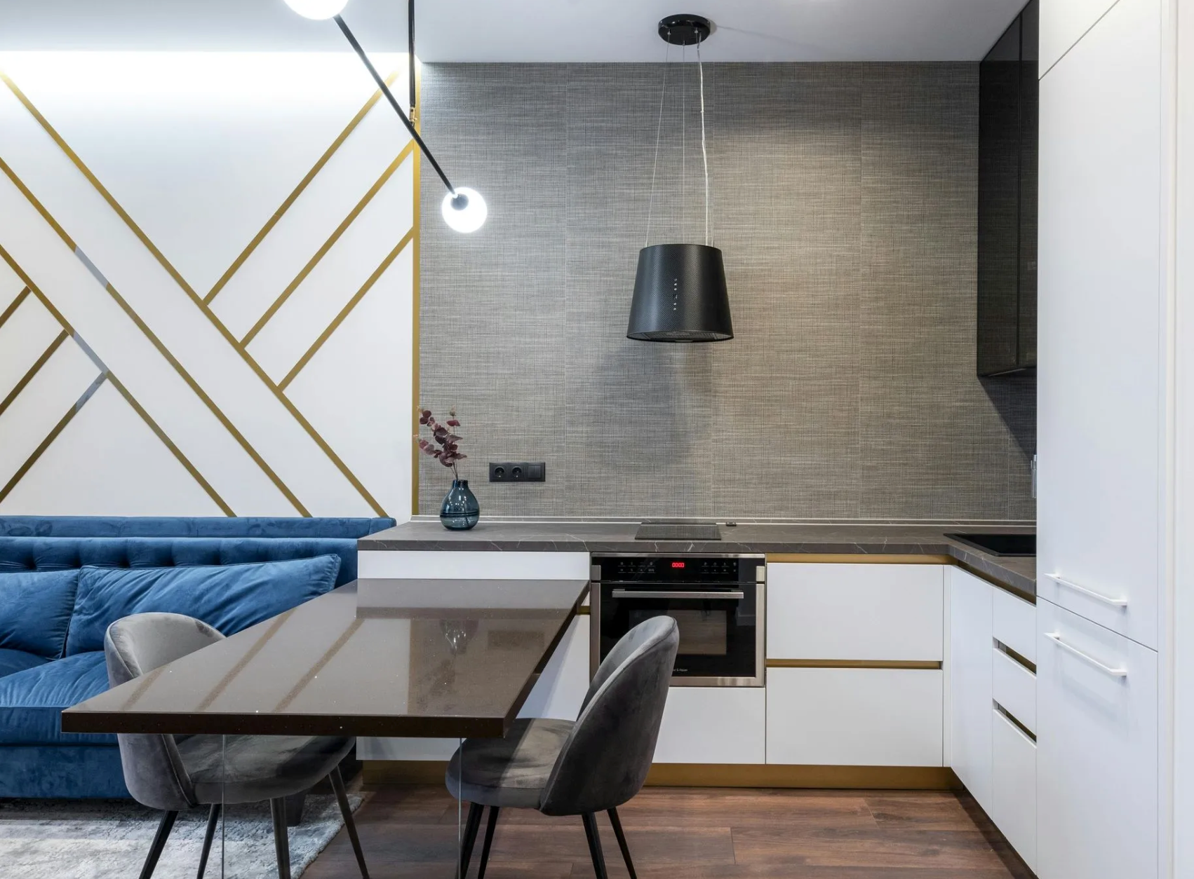 Modern kitchen with dining table and blue sofa, white cabinetry, dark countertop, and gold accents.