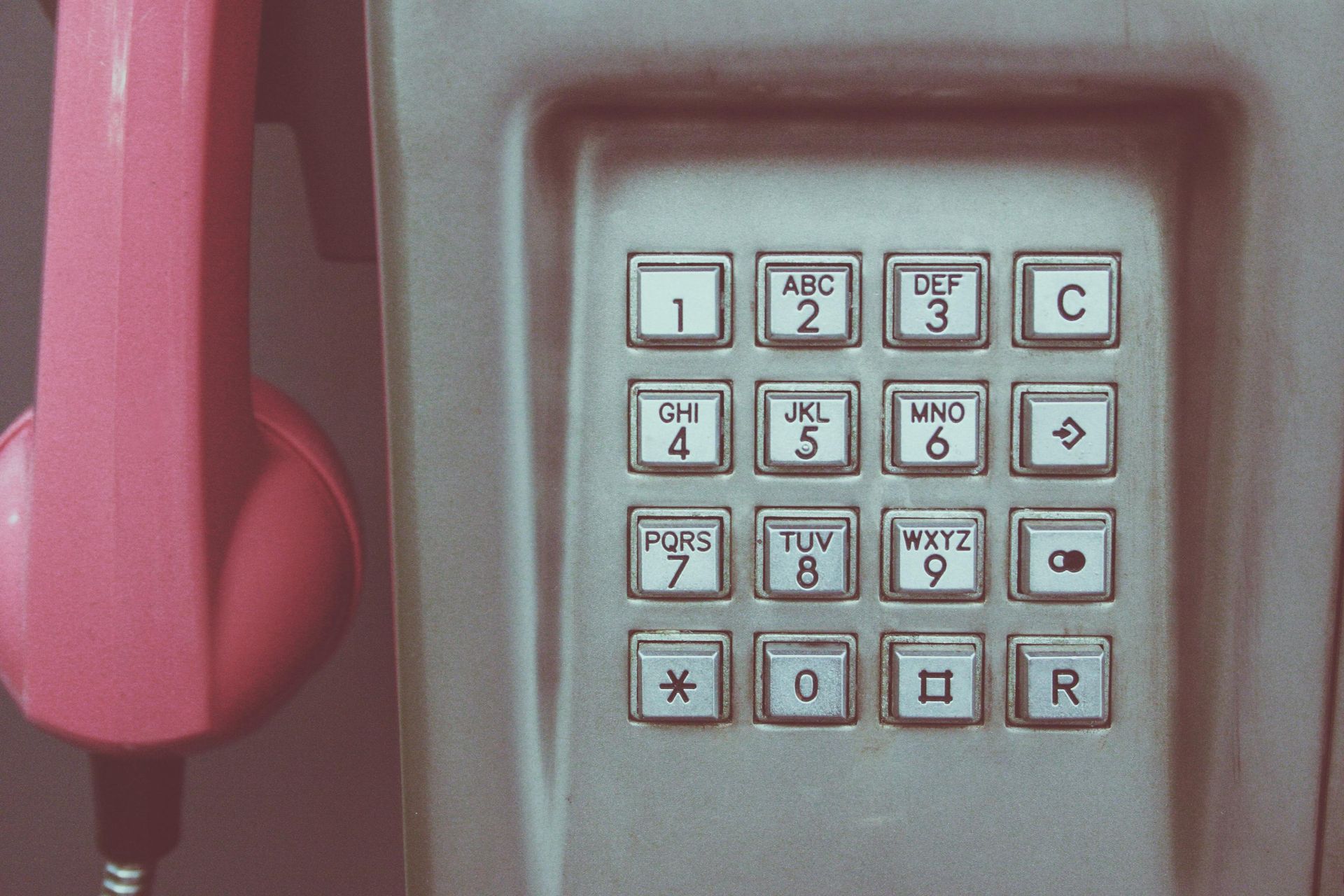 Close-up of a pink payphone receiver and keypad with white buttons and letters.