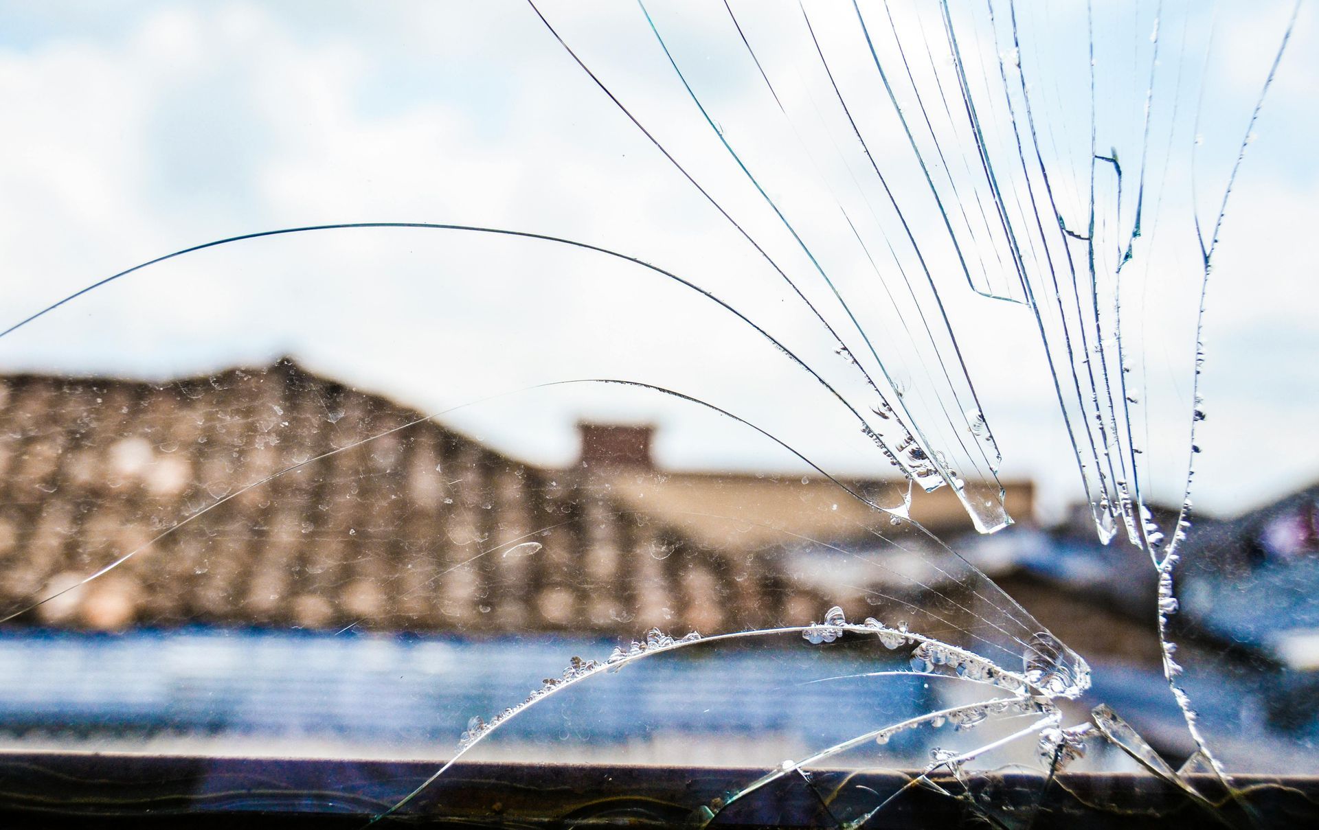 Cracked window pane with a blurred rooftop and blue sky in the background