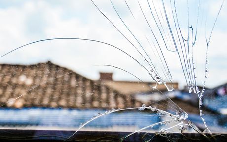 Cracked window pane with a blurred rooftop and blue sky in the background