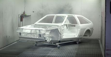 White car body shell in a paint booth, mounted on a stand during restoration or fabrication.