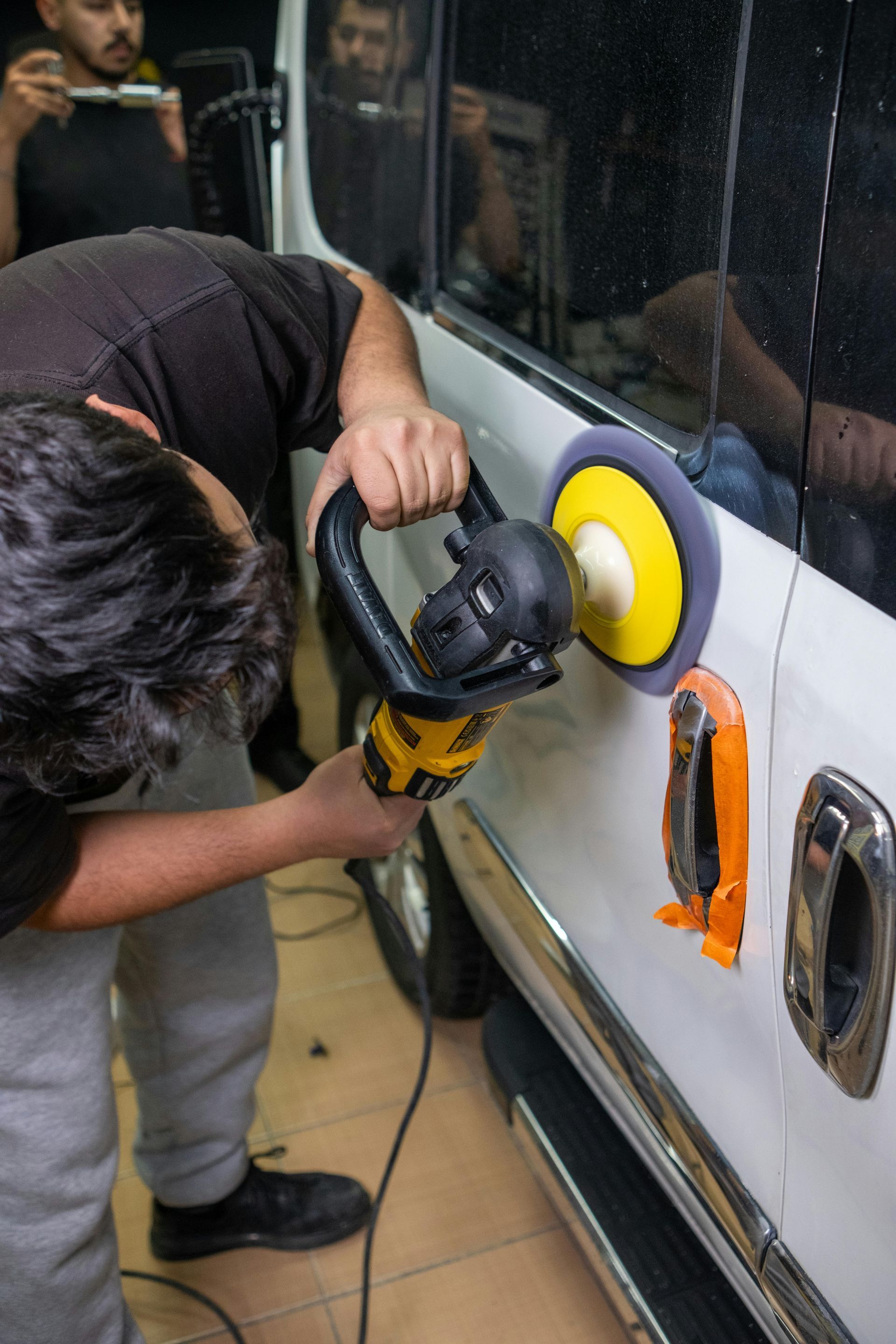 Person buffing a car door with a yellow polisher in a workshop