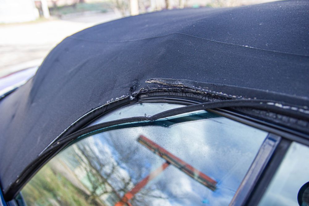 Close-up of a black car soft top with a torn seam above the side window