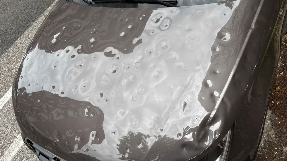 White hailstones covering a dark car hood outdoors