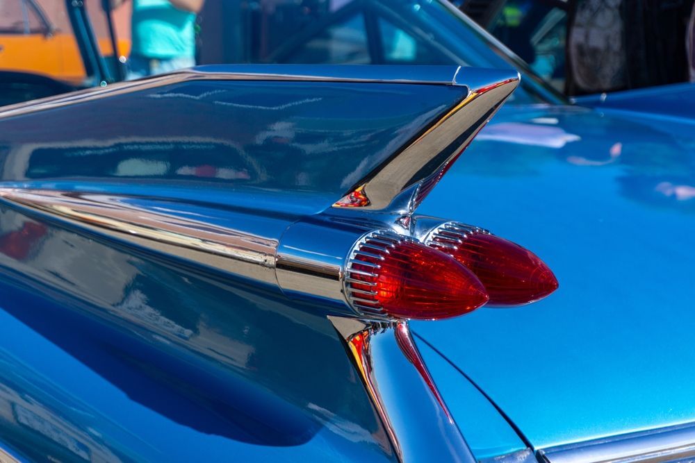 Close-up of a blue vintage car’s tail fin and red taillight chrome detail