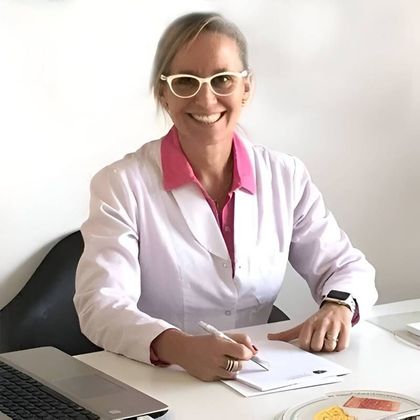 Una mujer con bata de laboratorio sonríe mientras escribe en un escritorio, con un teclado y un plato visibles.