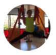 Mujer con camisa verde y pantalón negro haciendo yoga aéreo, con aparato rojo, piernas abiertas.