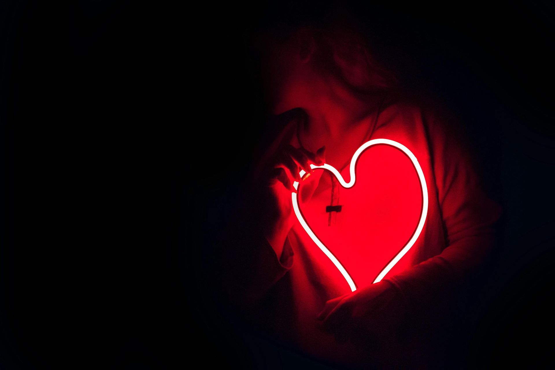 Persona que sostiene una luz roja brillante en forma de corazón en un entorno oscuro.