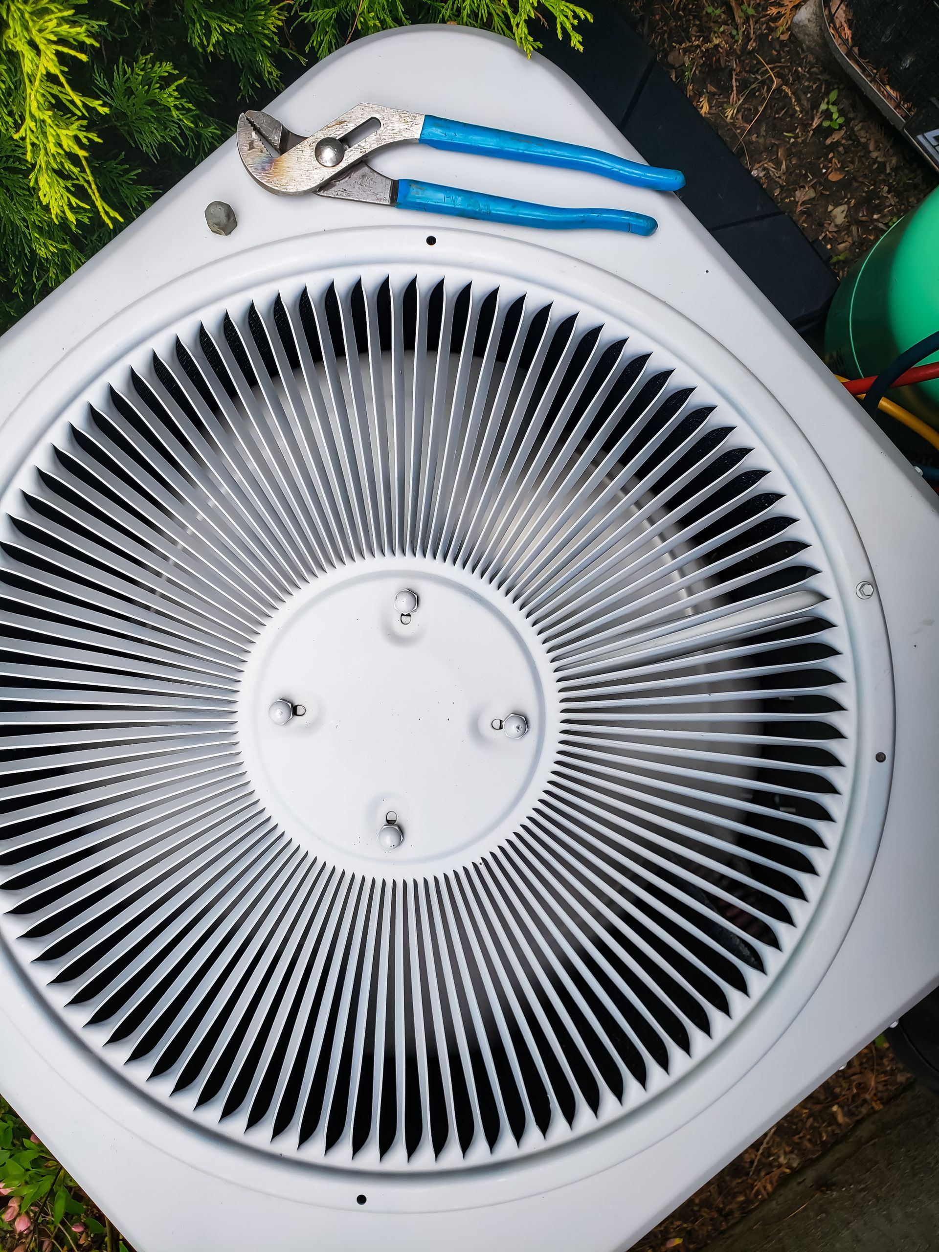 Top view of an outdoor air conditioner unit with blue-handled pliers resting on top