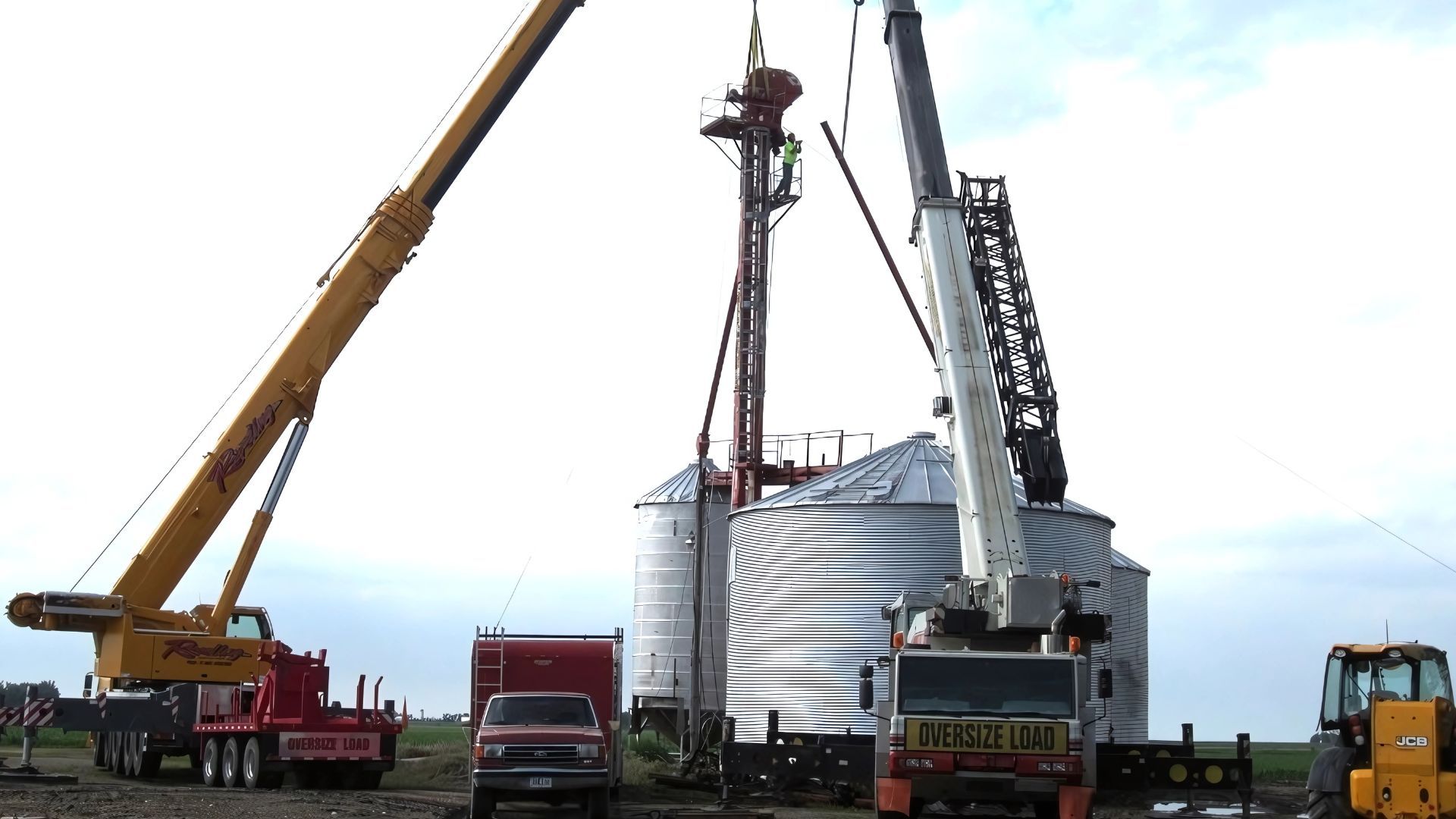 A large crane is lifting a silo in a field