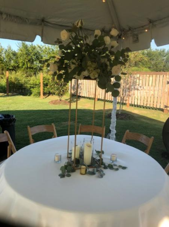 Round white table with candles and flowers under a canopy in a backyard garden