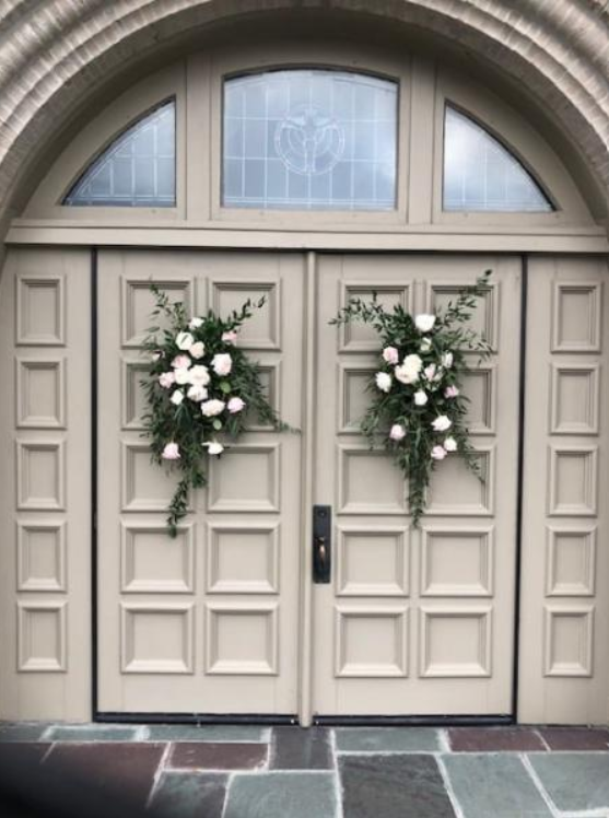 Double beige church doors with floral wreaths and arched stone entryway