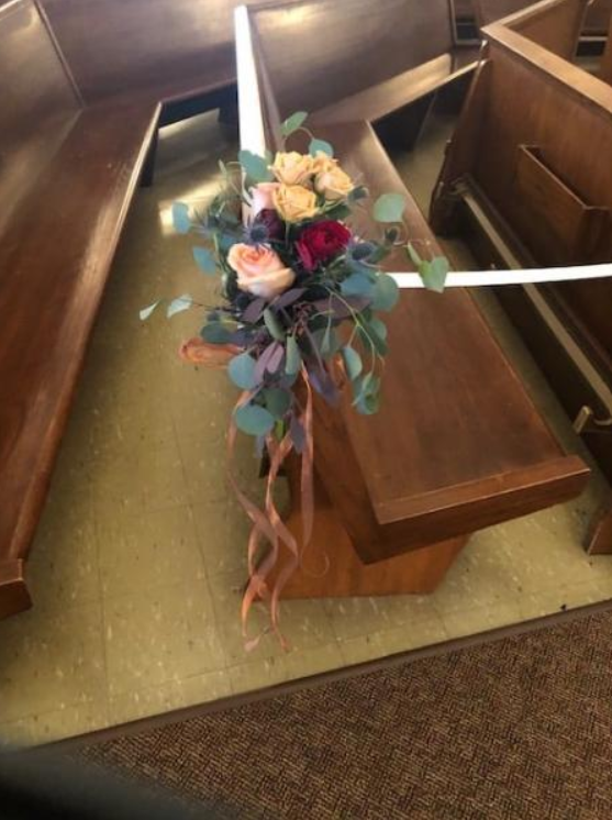 Floral bouquet in a church pew with white ribbons draped across wooden benches