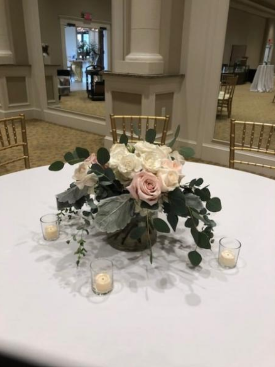 White and blush floral centerpiece with candles on a round table in a formal event hall