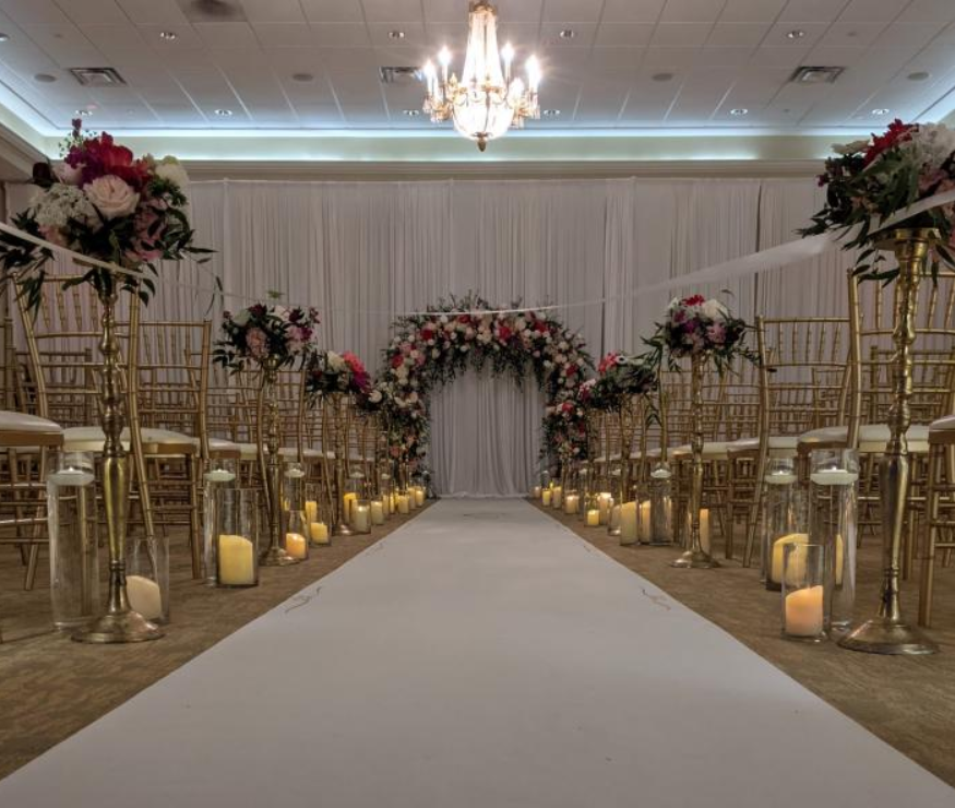 Elegant wedding aisle with gold chairs, white drapes, floral arch, and candlelit decor