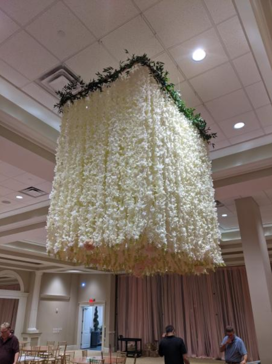 Large suspended floral chandelier with white hanging flowers in a banquet hall ceiling.