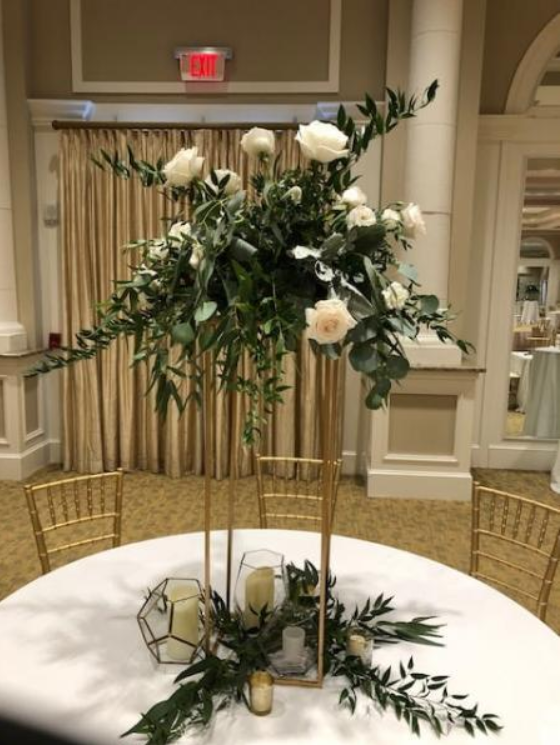 White floral centerpiece on a gold stand at a banquet table in a carpeted hall