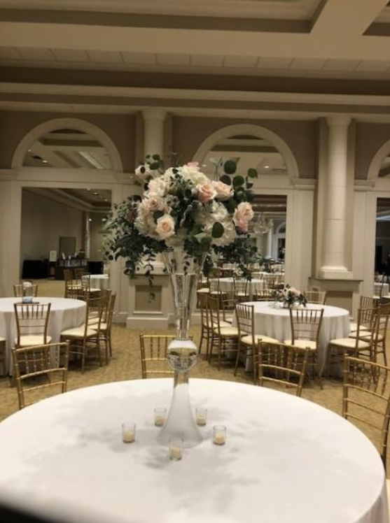 Elegant banquet hall with round tables and a tall floral centerpiece in soft pink and white.