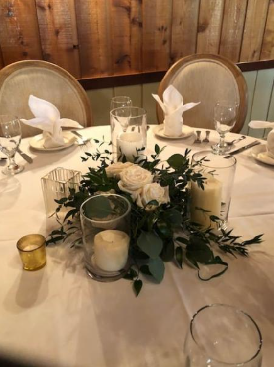 Elegant dinner table set with white napkins, candles, and greenery centerpieces in a wood-paneled room