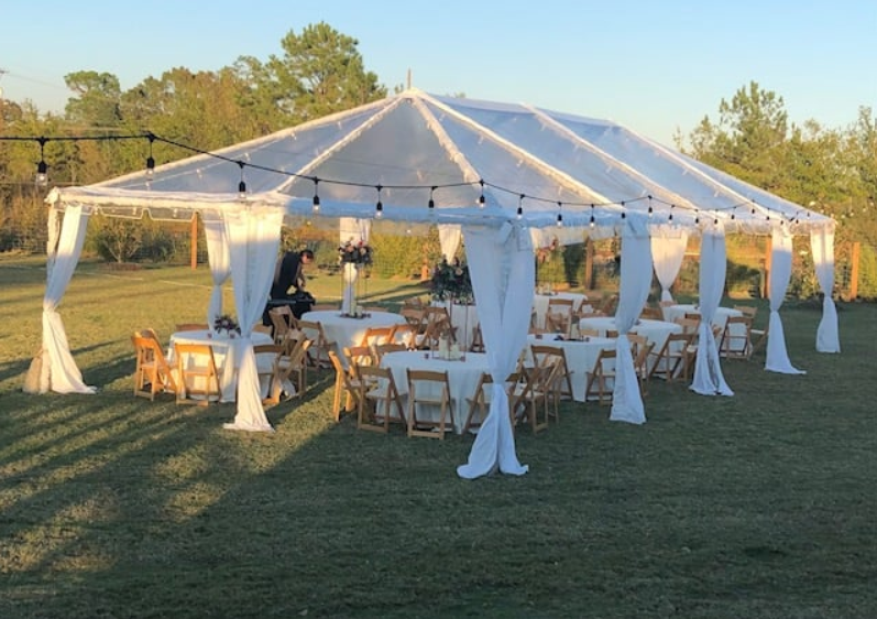White event tent with draped curtains and tables set up on a grassy lawn at sunset