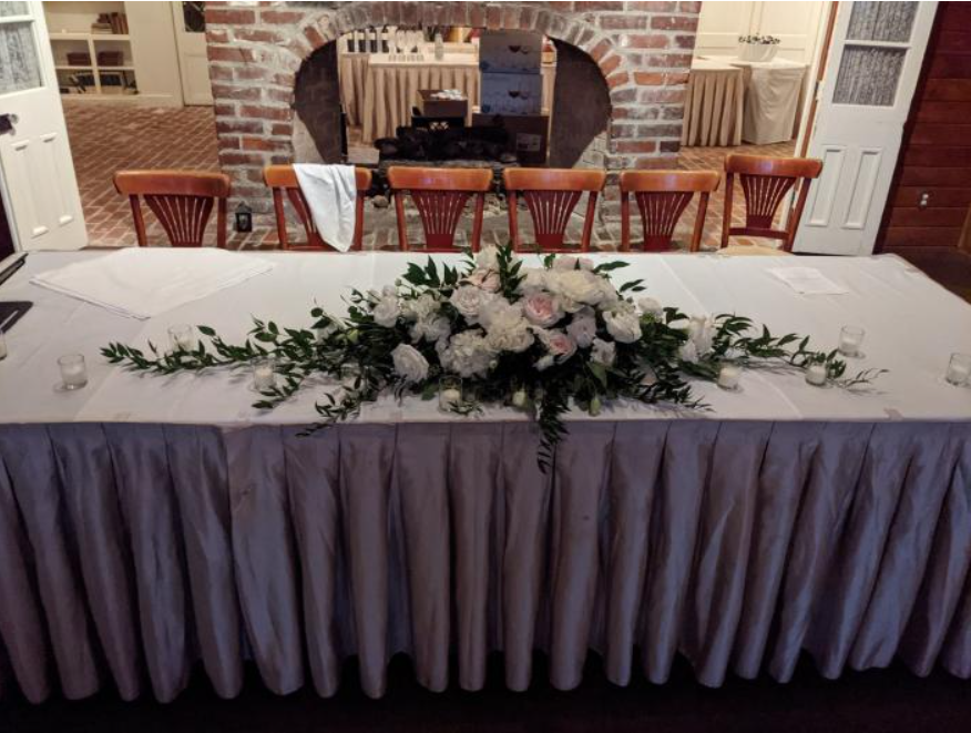 Wedding reception table with white cloth, lavender skirt, and white-and-green floral