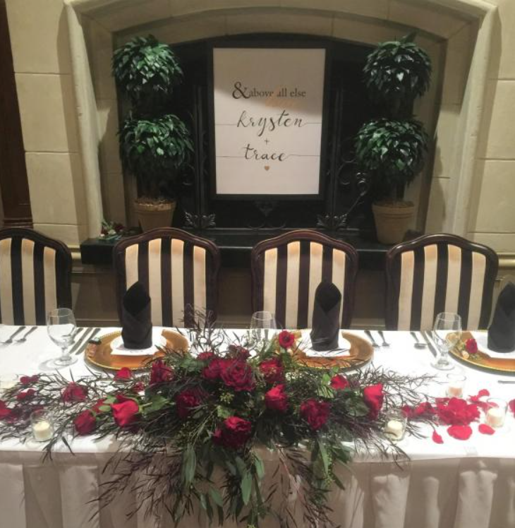Elegant banquet table with floral centerpiece and place settings in front of a stone fireplace and sign.