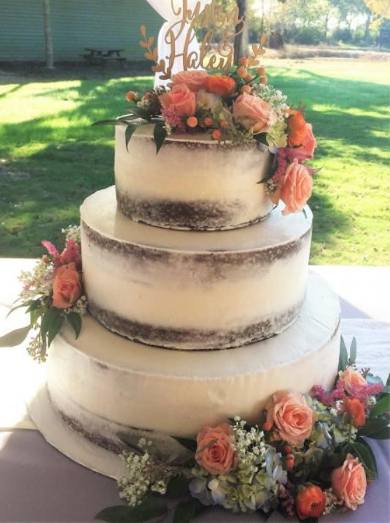Three-tier wedding cake with white frosting and peach floral decorations outdoors