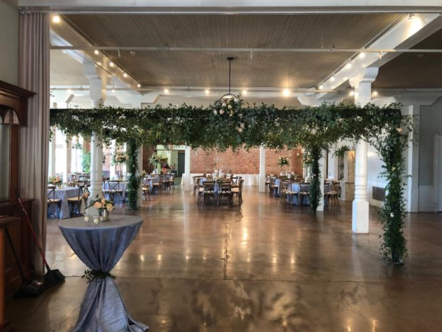 Elegant indoor venue with greenery arch, polished floor, and dining tables in a spacious hall