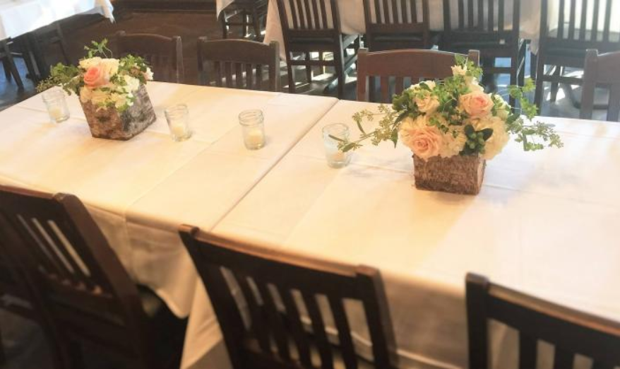 White-clothed dining table set with floral centerpieces and wooden chairs in a restaurant room