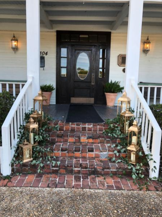 Brick front steps leading to a black front door with lanterns and potted plants on a porch
