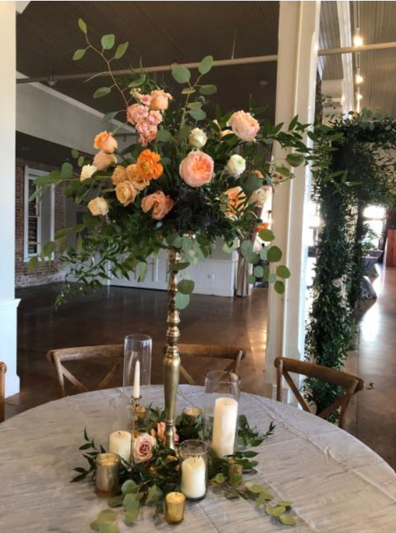 Tall floral centerpiece with peach roses on a round table in a banquet hall