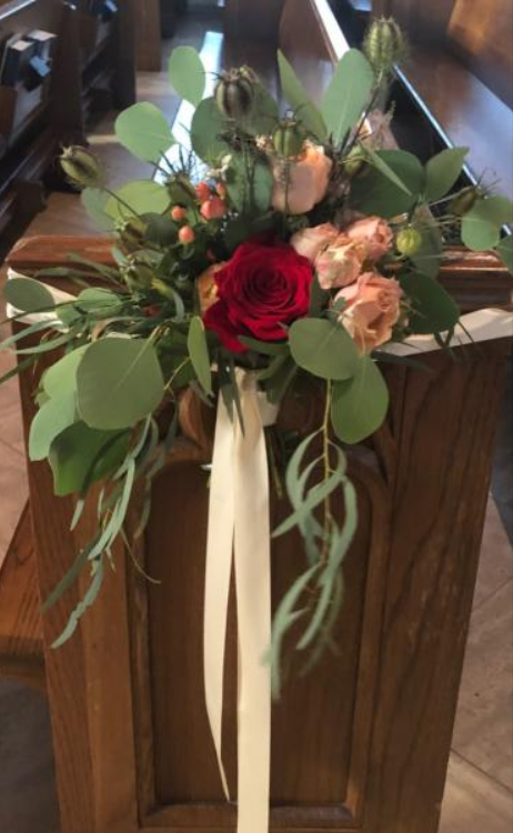 Bouquet of red and peach flowers with greenery and cream ribbons on a wooden podium