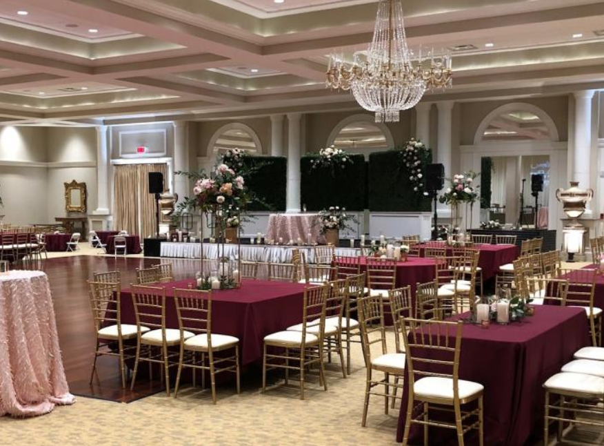 Elegant banquet hall with round tables, gold chairs, burgundy tablecloths, and chandeliers