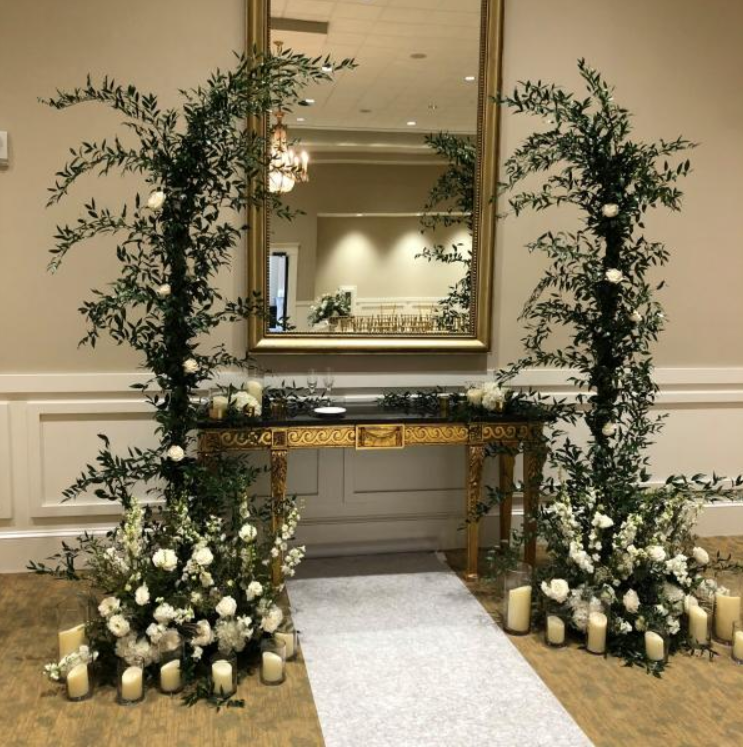 Elegant wedding entrance with white flowers, candles, greenery, and a mirrored table on a carpeted aisle