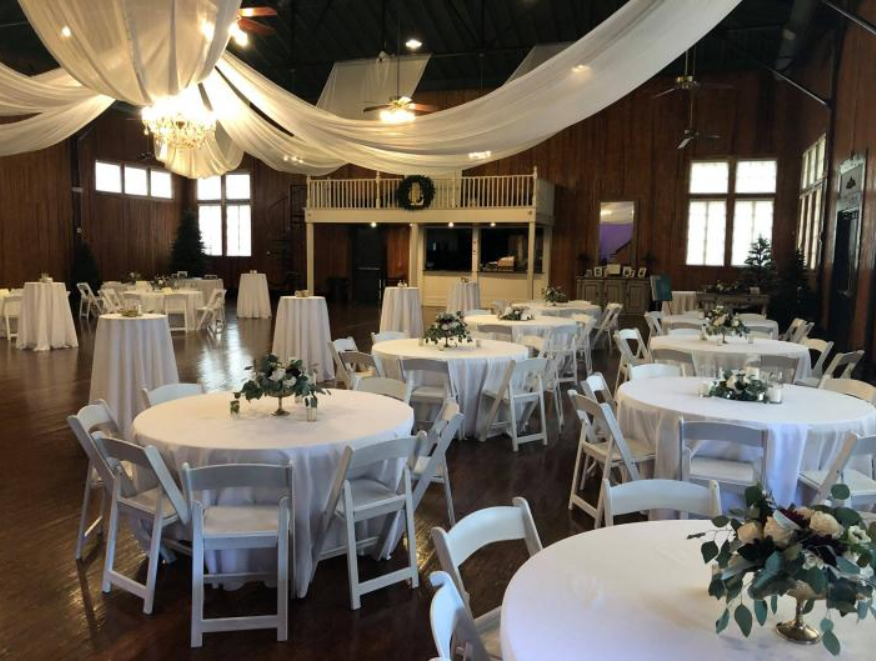 Elegant banquet hall with round tables, white chairs, and draped white fabric ceiling decor