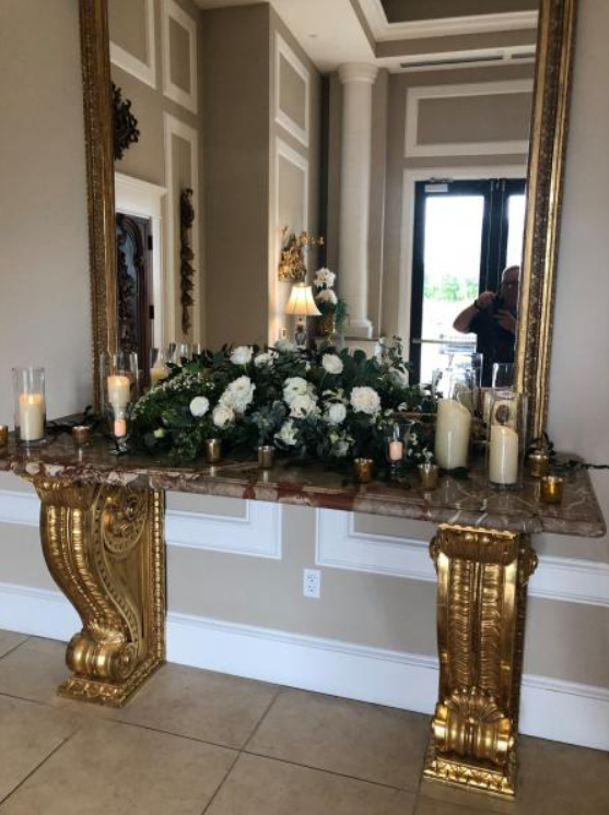 Elegant console table with gold legs, mirror, and white floral arrangement in a hallway