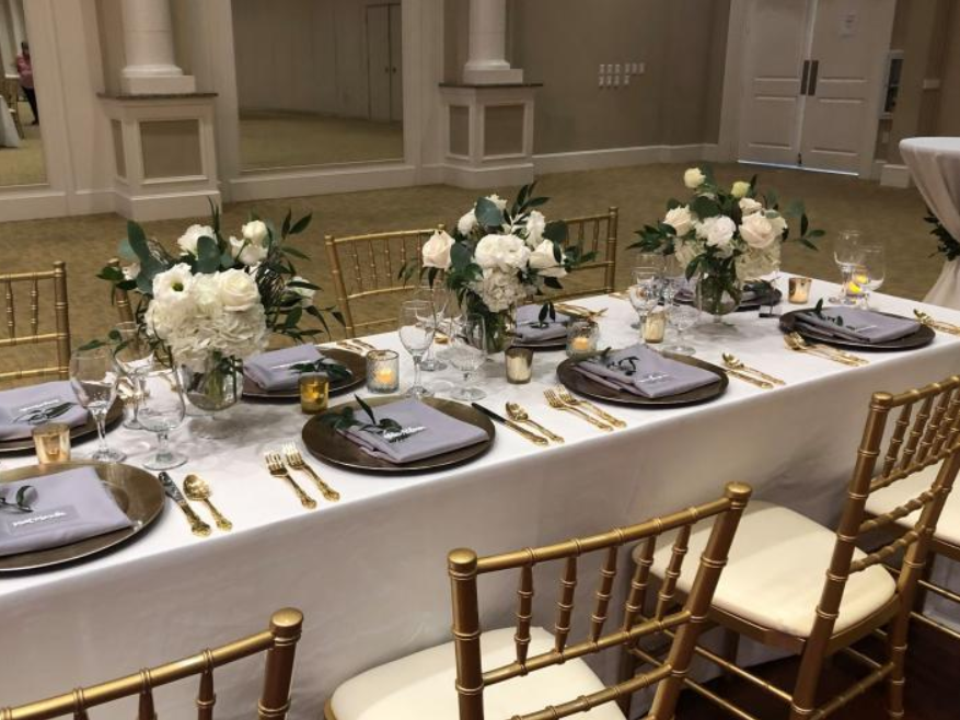 Elegant banquet table set with white floral centerpieces, gold accents, and place settings in a formal hall