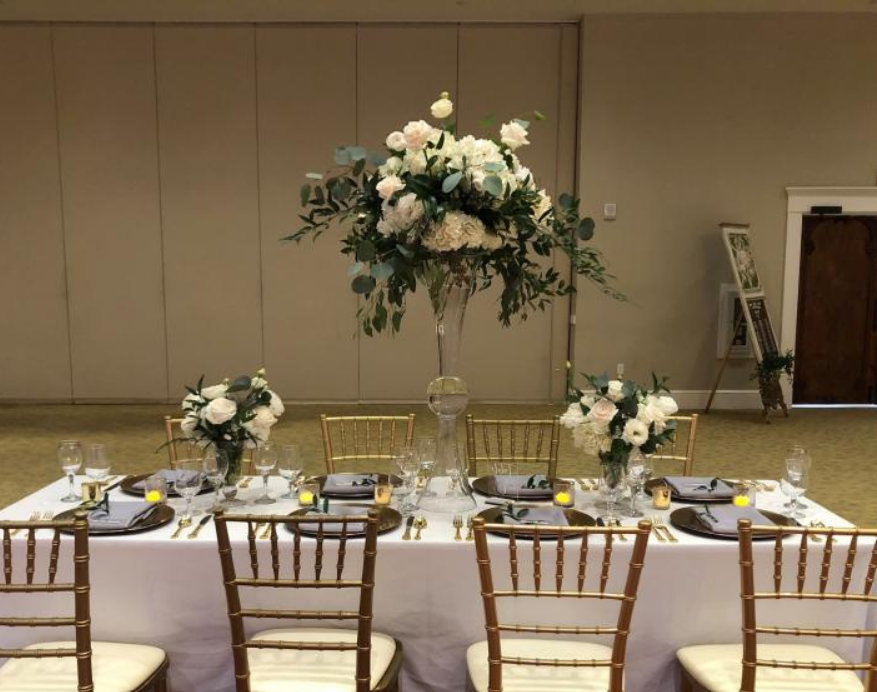 Elegant banquet table with white floral centerpieces and gold chairs in a reception hall