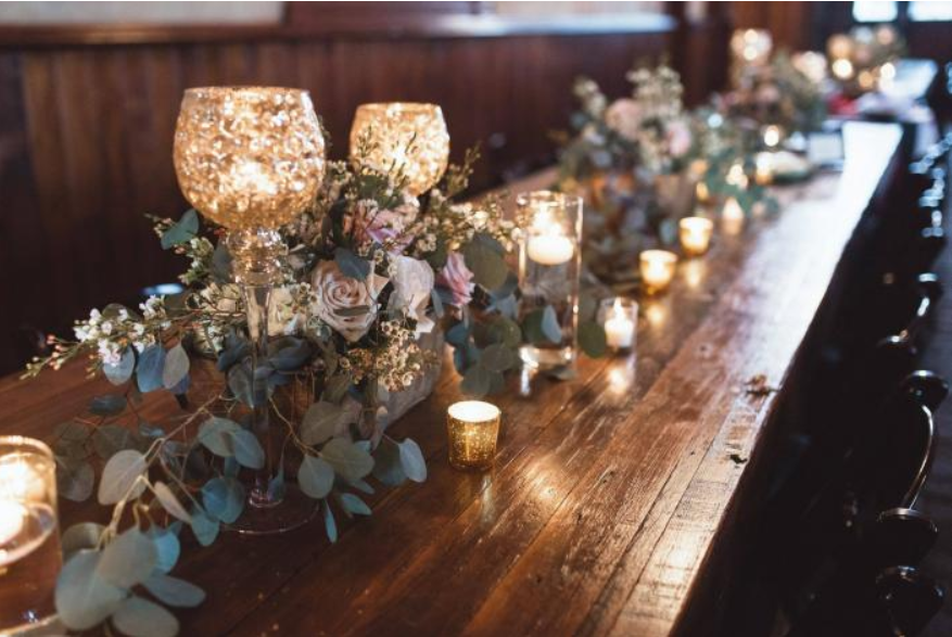Candlelit rustic banquet table with floral greenery and gold votive holders