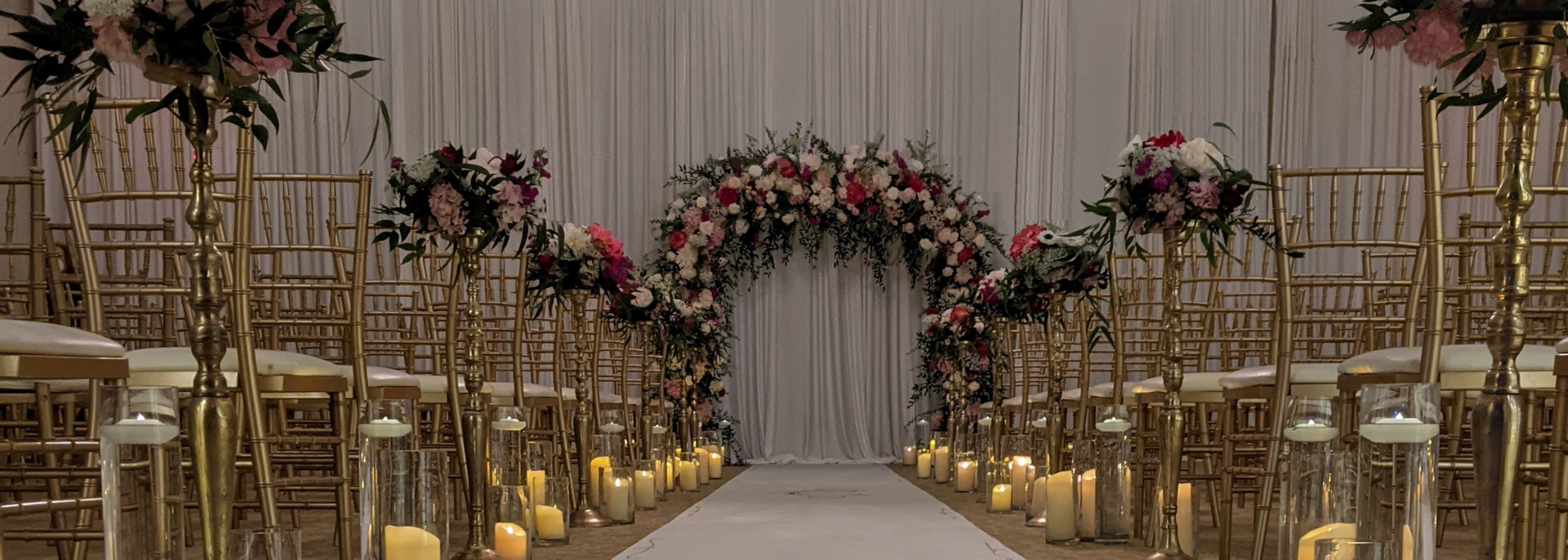 Elegant wedding ceremony aisle with white chairs, floral arch, and warm candlelight