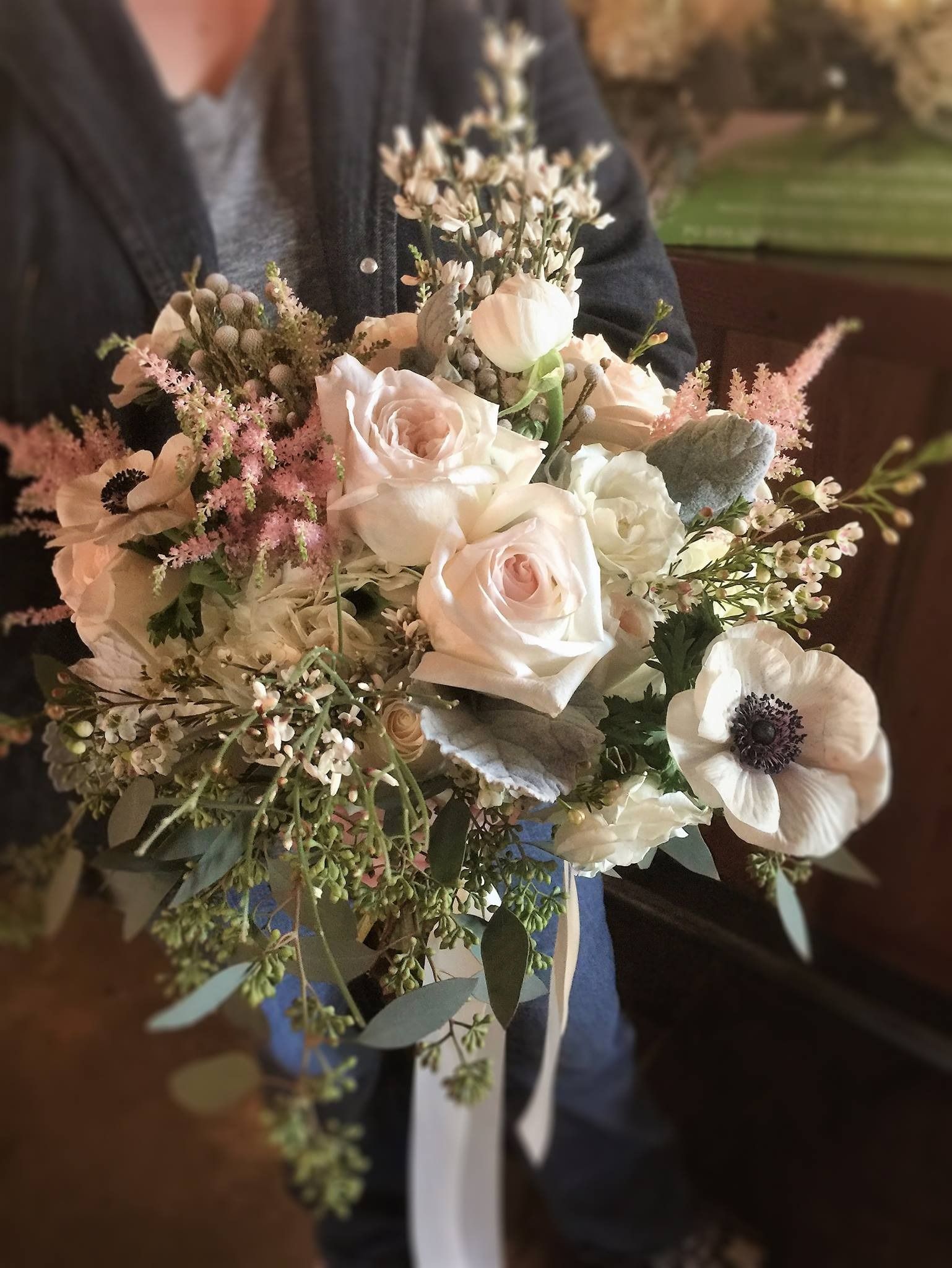 Handheld bouquet of pale pink and white flowers with greenery and soft pink accents