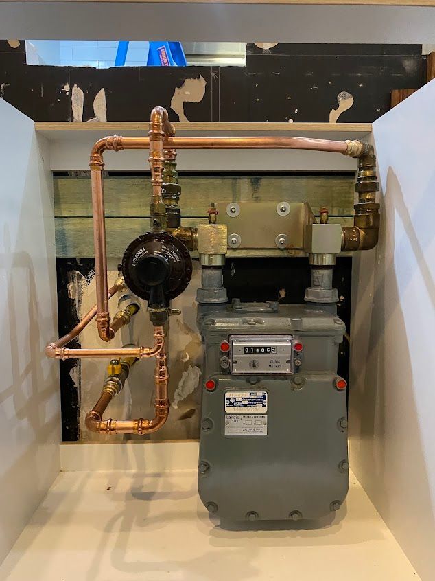A Gas Meter Is Sitting Inside A Cabinet with Copper Pipes Attached to It — Lakesway Plumbing and Gas in Forster, NSW