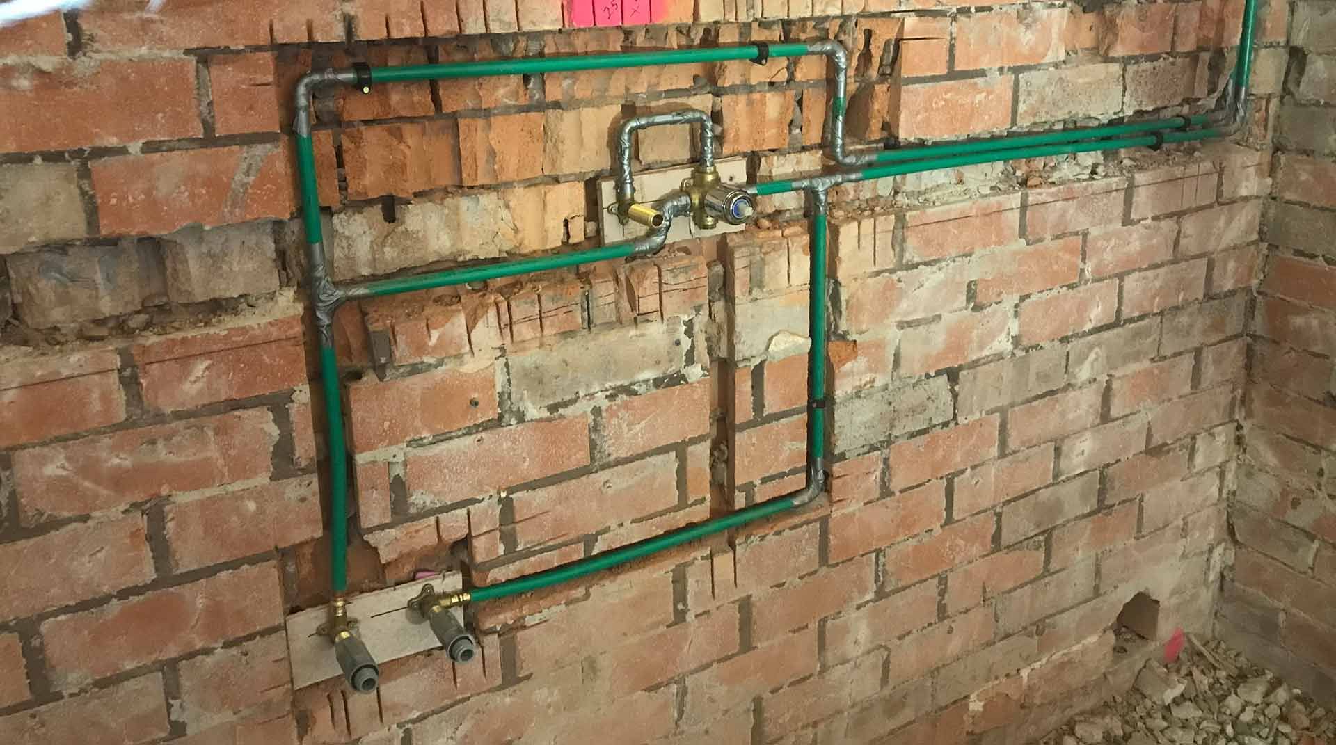 A Brick Wall With Green Pipes Coming Out Of It — Lakesway Plumbing and Gas in Forster, NSW