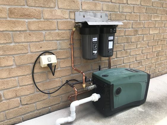 A Brick Wall with A Water Pump Attached to It — Lakesway Plumbing and Gas in Forster, NSW