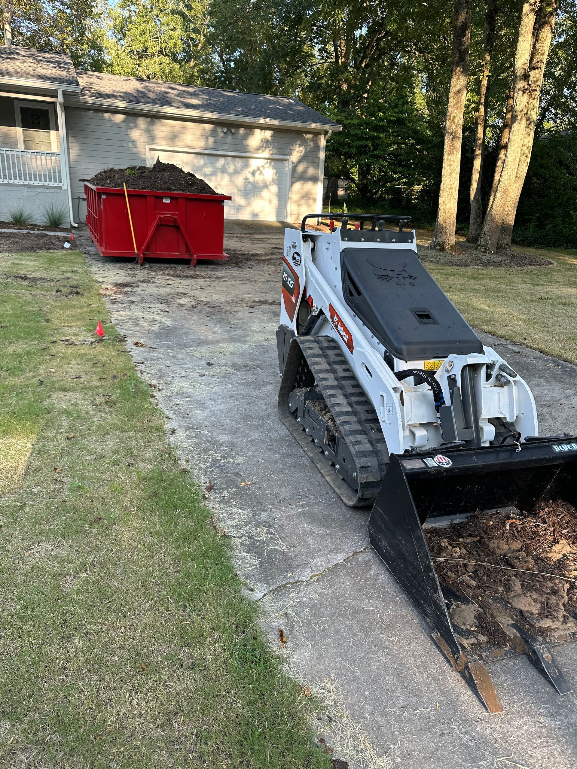 Brush Removal A bulldozer is digging a hole in the ground in front of a house.