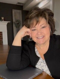 A woman wearing a black jacket and a zebra print shirt is smiling for the camera.