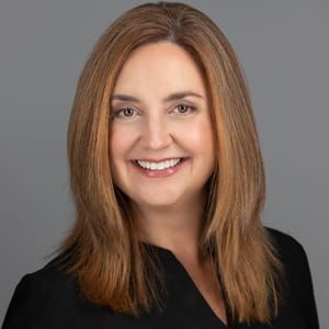 A woman with long brown hair is smiling and wearing a black shirt.