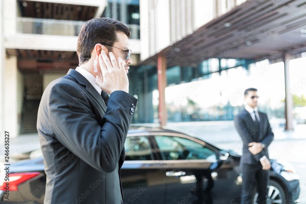 Security guard in black uniform using a handheld radio outside a glass building.