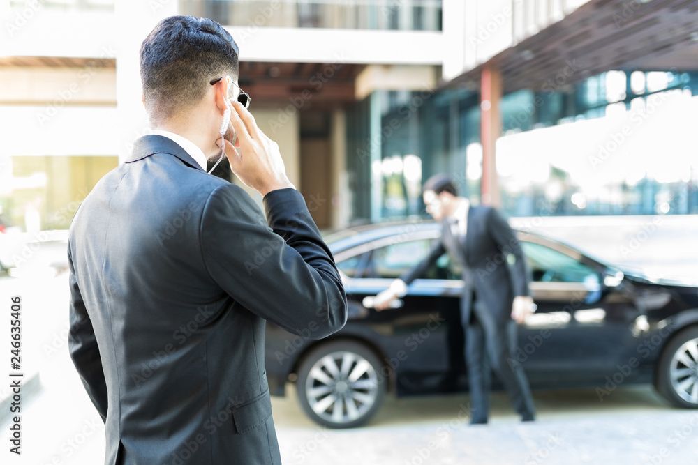 Security guard in black uniform and cap using a walkie-talkie outdoors.